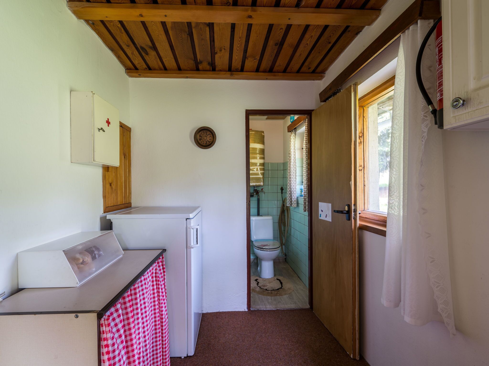 Una cocina compacta con refrigerador, lavamanos y techo de madera.
