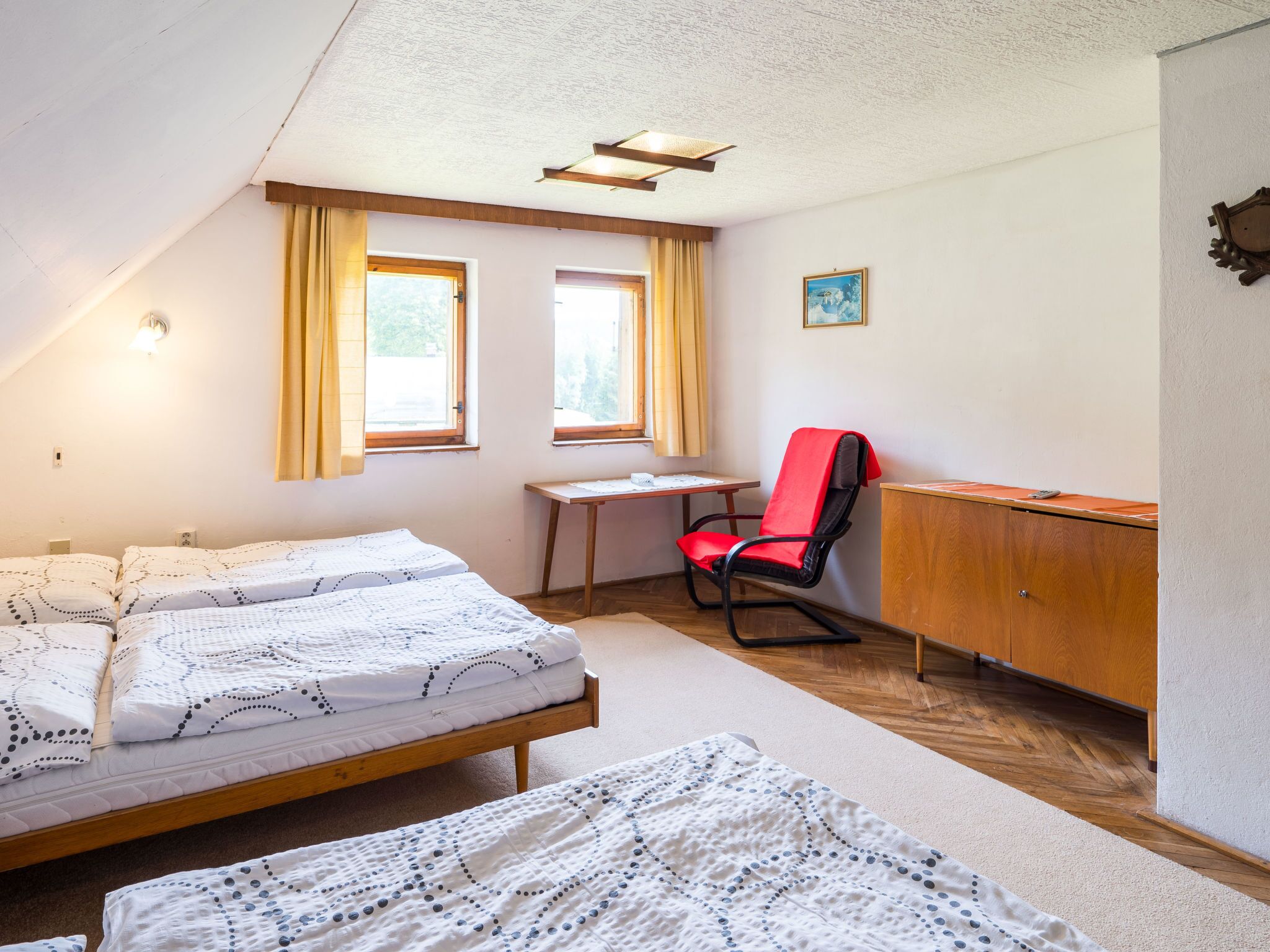 A small, well-lit room with two beds, a desk, a chair, and a cabinet.