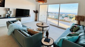 Un salon moderne avec un canapé gris, une table ronde en bois et un grand téléviseur.