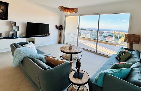 A modern living room with a grey sofa, a round wooden table, and a large TV.