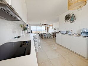 A modern kitchen with a central island, white cabinetry, and a view of the outdoors. - Appartement de 2 Chambres Pour 4 Personnes (L'Île-Rousse)