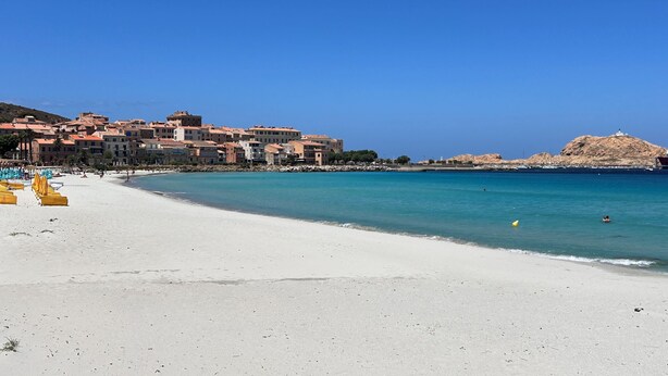 Une ville côtière dotée d’une plage de sable, d’une mer d’un bleu limpide et de bâtiments aux toits recouverts de tuiles rouges.