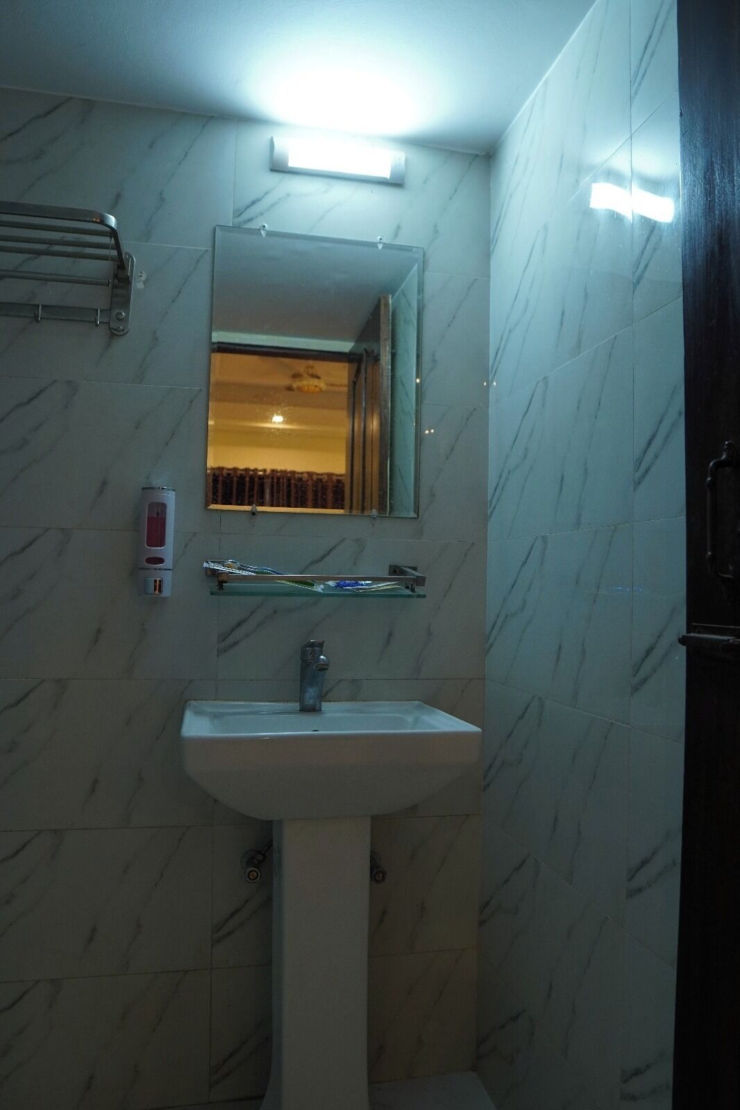 Un baño con un lavamanos blanco, un espejo y un perchero para toallas.