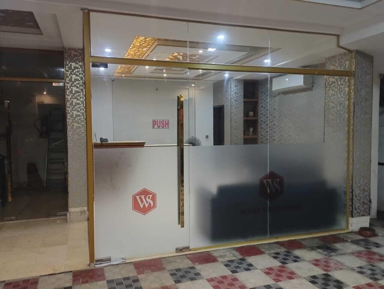 A hotel reception area with a glass door, a push bar, and a logo on the door.