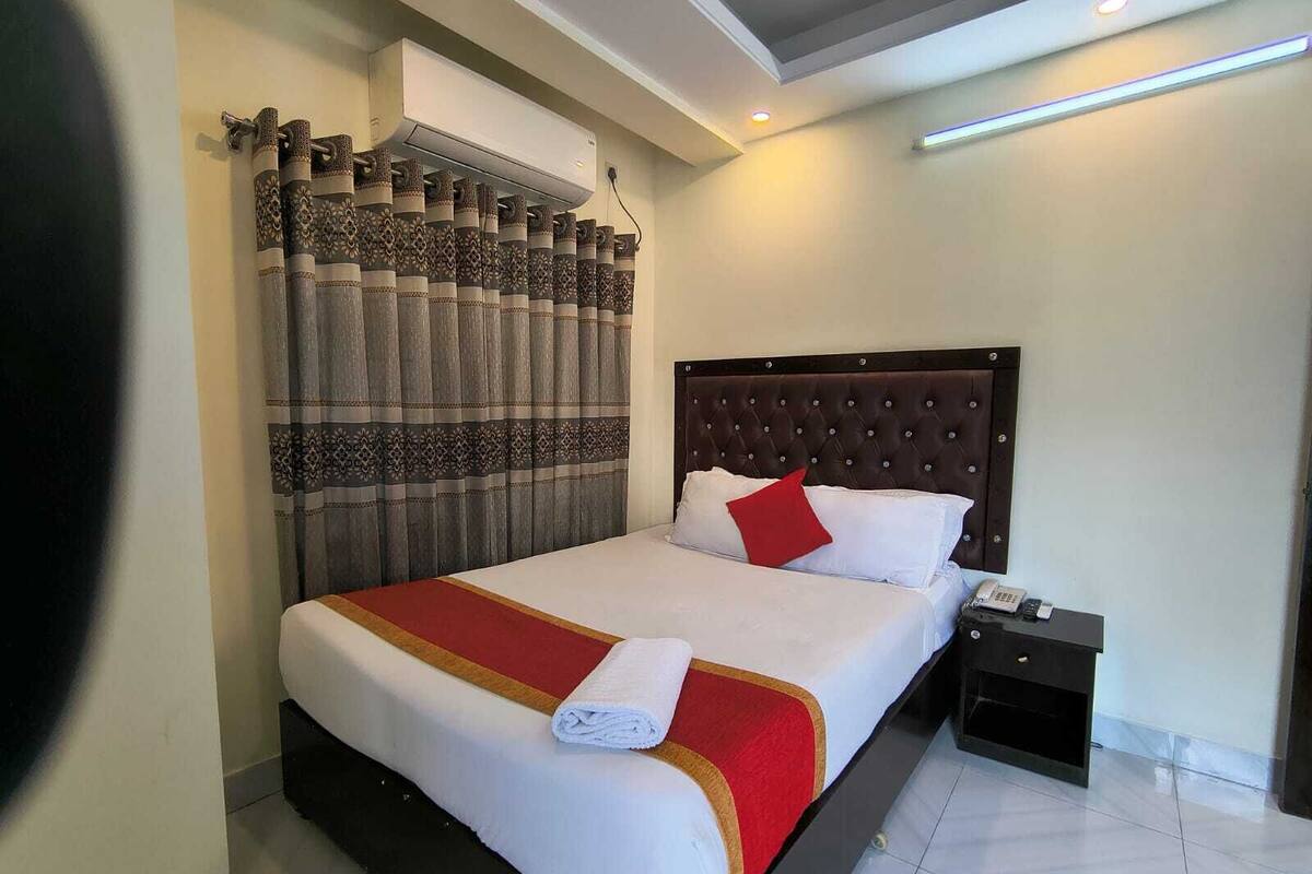 Ein Hotelzimmer mit einem großen Bett, einem Nachttisch mit Telefon und einer Wand-Klimaanlage.