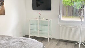Une chambre à coucher comprenant un lit, un téléviseur fixé au mur, une vitrine et une fenêtre donnant sur un paysage verdoyant.