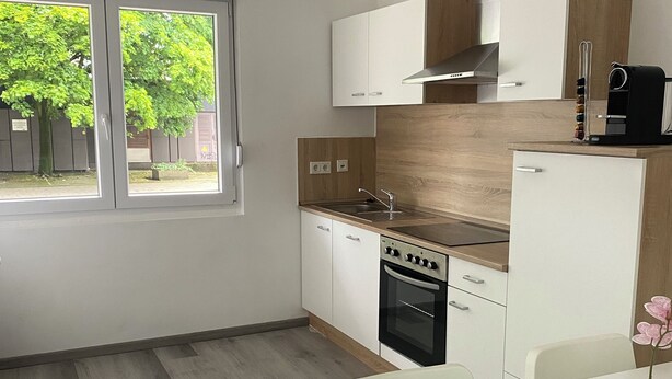 Une cuisine moderne avec des meubles blancs, un plan de travail en bois et un four encastré. Une fenêtre laisse entrer la lumière naturelle et offre une vue sur la verdure environnante.