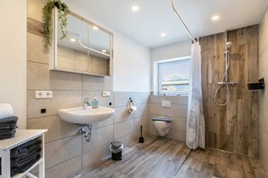 A modern bathroom with a sink, mirror, toilet, and shower. - Apartment 'Deichperle An Der Eider' with Private Terrace, Private Garden and Wi-Fi (Tönning)