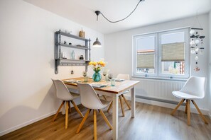 A modern kitchen with a dining table, chairs, and a window with blinds. - Apartment 'Deichperle An Der Eider' with Private Terrace, Private Garden and Wi-Fi (Tönning)