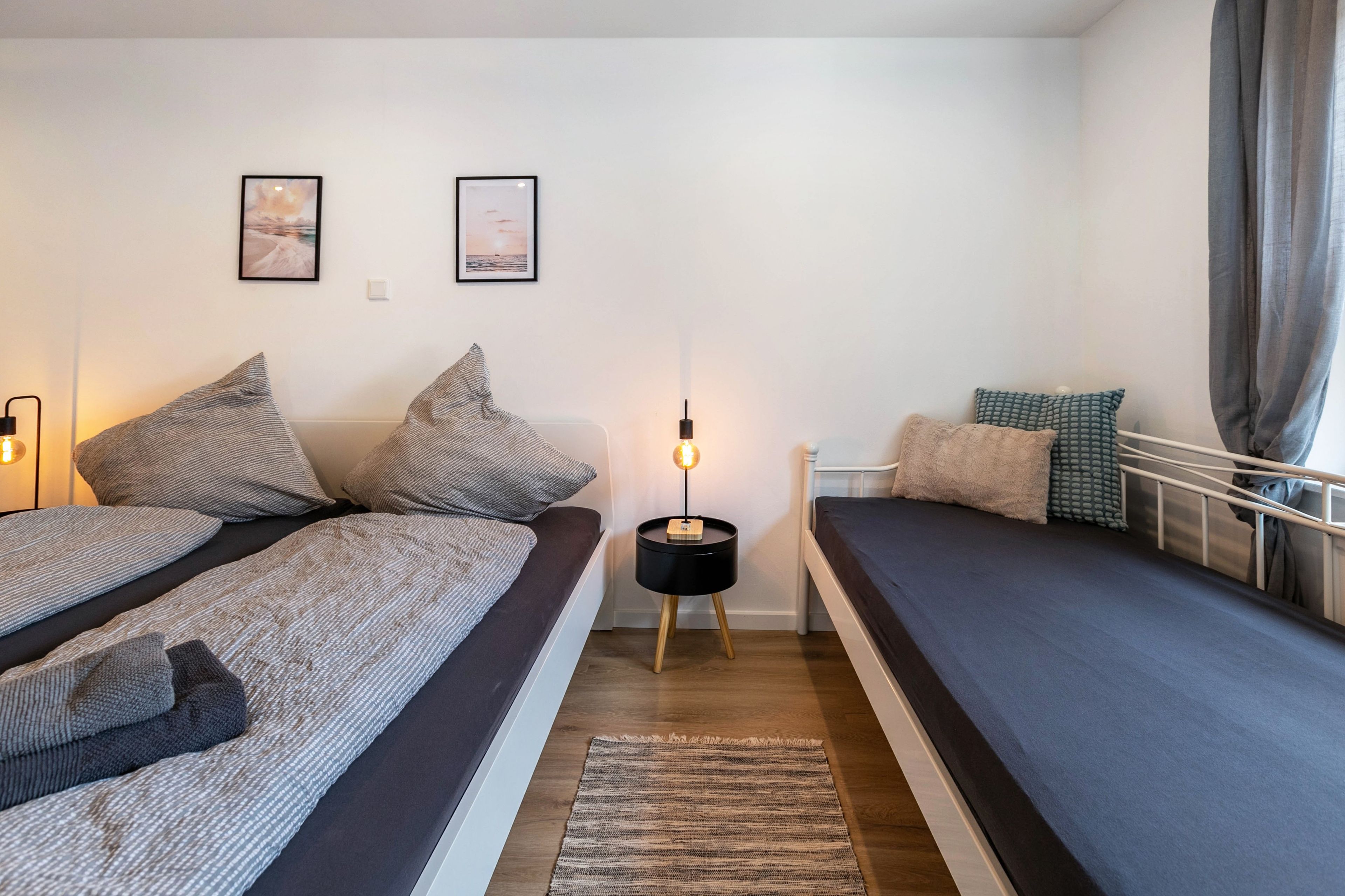 Een slaapkamer met twee bedden, een nachtkastje met een lamp en twee ingelijste foto’s aan de muur.