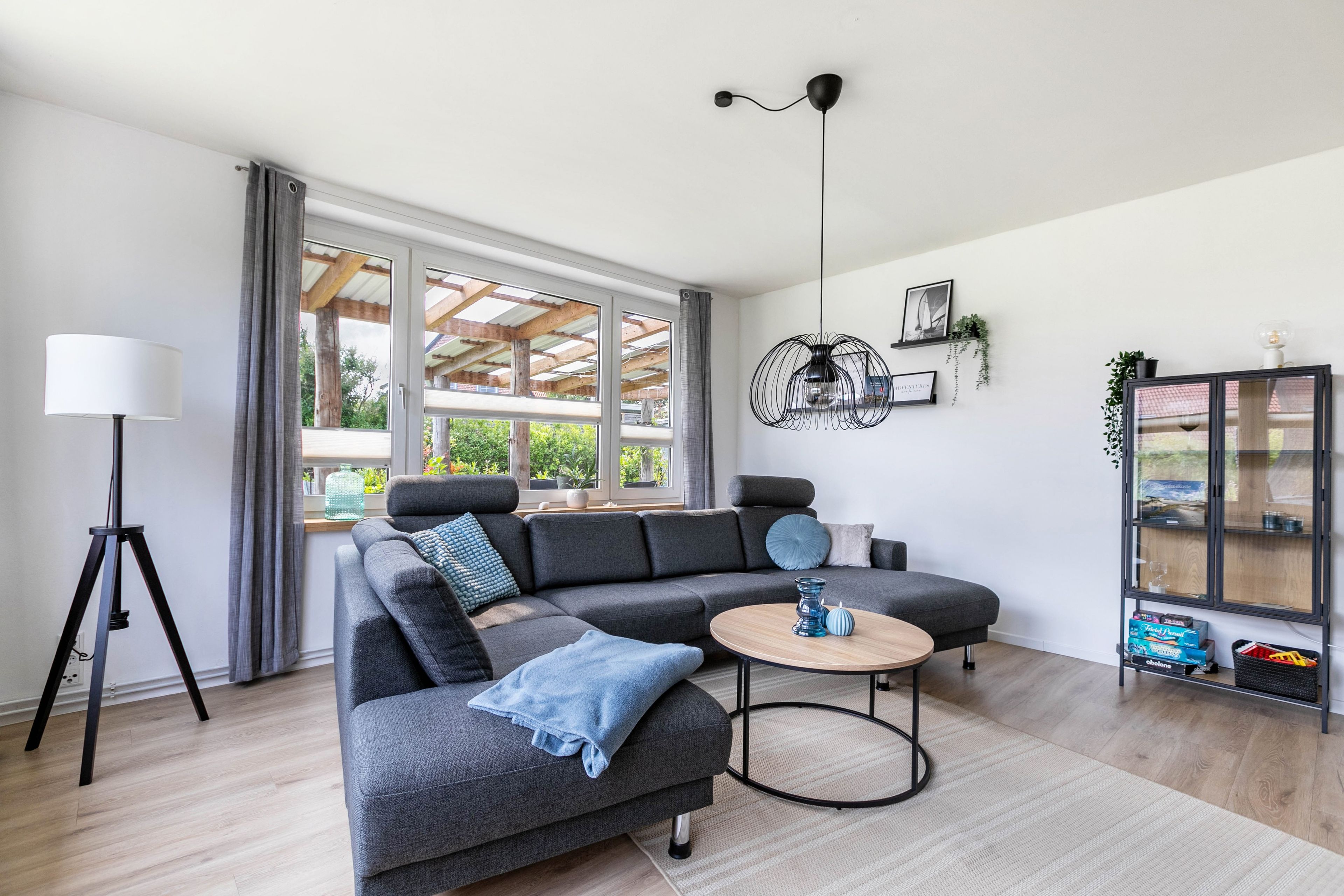 Un salon moderne avec un canapé d’angle, une lampe sur pied, une table basse ronde et une bibliothèque.