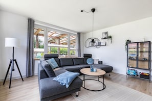 A modern living room with a sectional sofa, a floor lamp, a round coffee table, and a bookshelf.