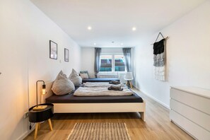 A modern bedroom with a bed, bedside tables, a lamp, and a view of the outside. - Apartment 'Deichperle An Der Eider' with Private Terrace, Private Garden and Wi-Fi (Tönning)