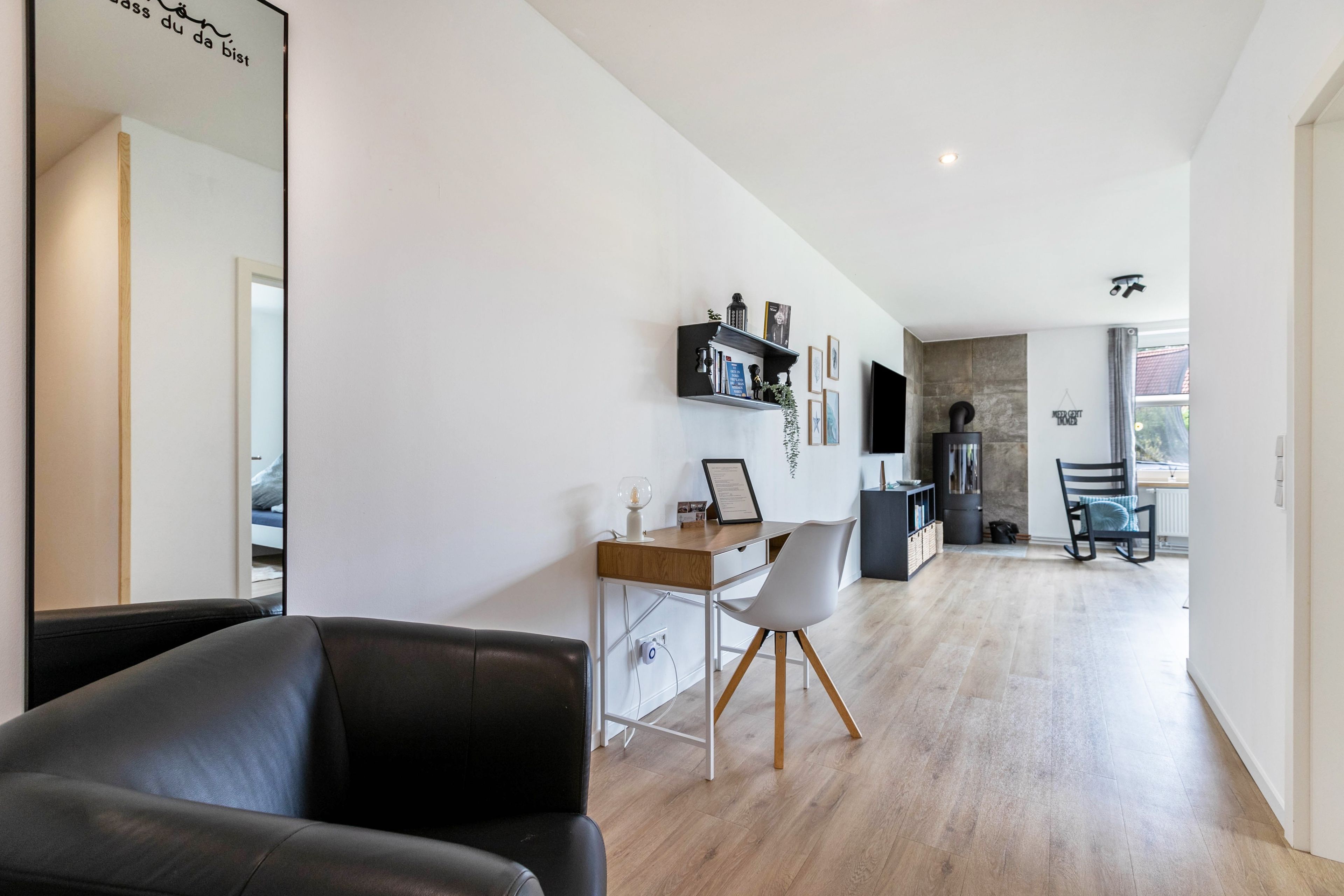 A modern living room with a black leather sofa, a wooden dining table, and a kitchen area with a stove.