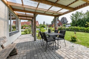 A covered patio area with a table and chairs, a wooden bench, and a view of a residential street. - Apartment 'Deichperle An Der Eider' with Private Terrace, Private Garden and Wi-Fi (Tönning)