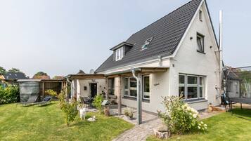 A two-story house with a sloped roof, a covered patio, and a well-maintained lawn.