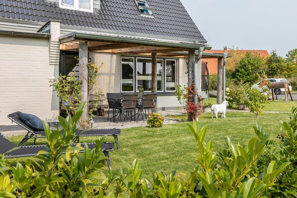 A house with a covered patio, outdoor seating, and a lawn with a sheep sculpture.