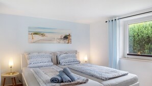 A double bed with patterned bedding, a bedside lamp, and a beach-themed painting on the wall. - Apartment 'Ferienanlage Kappeln-Kopperby' with Private Terrace, Private Garden and Wi-Fi (Kappeln Kopperby)