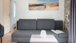 A modern living room with a grey sofa, a wooden coffee table, and a beach-themed painting on the wall. - Apartment 'Ferienanlage Kappeln-Kopperby' with Private Terrace, Private Garden and Wi-Fi (Kappeln Kopperby)