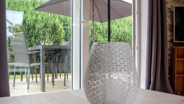 A table with a glass vase, a bottle, and a glass, with outdoor furniture and a view of greenery. - Apartment 'Ferienanlage Kappeln-Kopperby' with Private Terrace, Private Garden and Wi-Fi (Kappeln Kopperby)