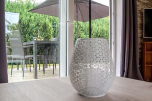 Una mesa con un florero de vidrio, una botella y un vaso, mobiliario exterior y vistas a la vegetación.