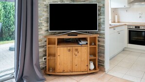 A modern living room with a flat-screen TV on a wooden stand, a kitchen area with white cabinets, and a stone-patterned wall. - Apartment 'Ferienanlage Kappeln-Kopperby' with Private Terrace, Private Garden and Wi-Fi (Kappeln Kopperby)
