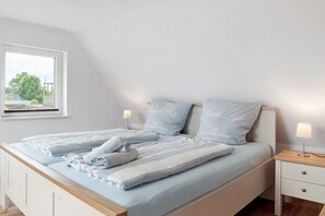 Une chambre à coucher avec un lit, deux tables de chevet, une fenêtre et une vue sur la verdure.