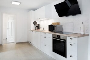 Une cuisine moderne avec des meubles blancs, un four encastré, un four à micro-ondes et une machine à café.
