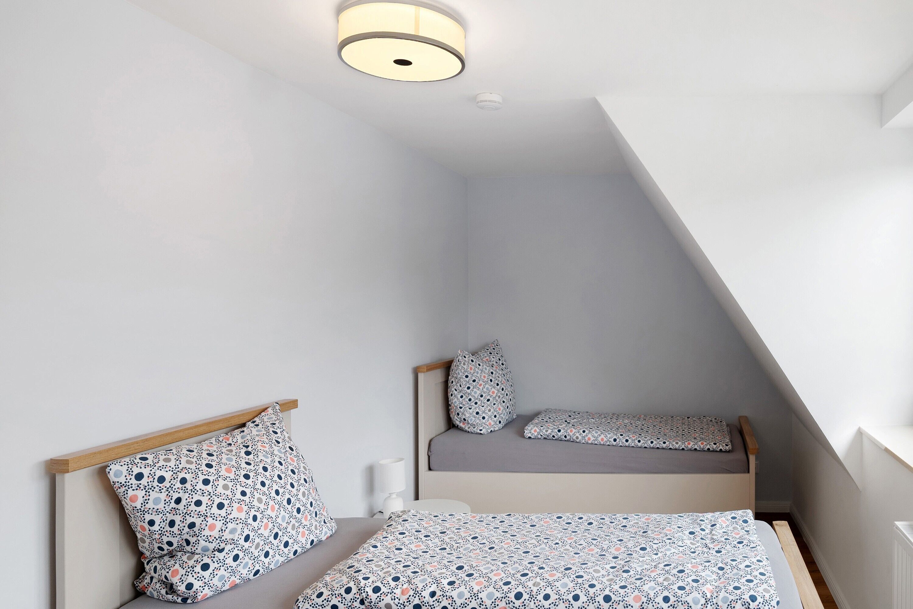 A bedroom with two beds, a ceiling light, and a sloped ceiling.
