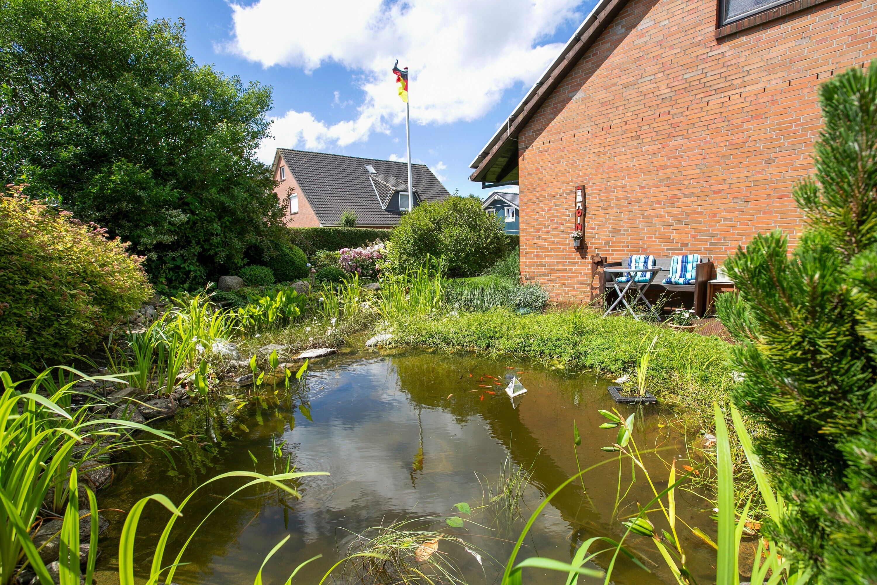 Ein Teich mit Wasserpflanzen, ein Backsteinhaus und eine Flagge.