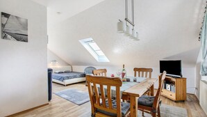 Quarto estilo loft com área de jantar, sofá, TV e claraboia.