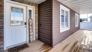 Eine Holzterrasse mit Fußmatte, eine Steinmauer und ein Haus mit brauner Holzverkleidung.