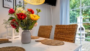 Ein Esstisch mit Blumen in einer Vase, Korbstühle und einer Korrespondierenden Lampe.