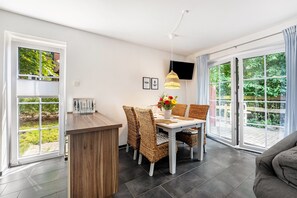 A modern kitchen with a dining area, large windows, and a flat-screen TV.