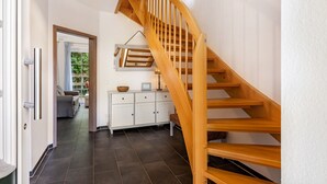 Eine Holztreppe führt zu einer Zwischenebene mit einem weißen Schrank und einer Pendelleuchte.