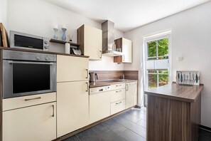 A modern kitchen with built-in appliances, a wooden countertop, and a view of greenery outside.