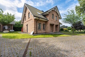 A two-story brick house with a tiled roof, a front lawn, and a paved driveway.