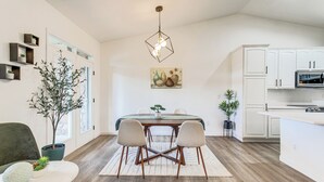 A modern kitchen with white cabinets, a dining area with a wooden table and chairs, and a hanging light fixture. - Seasonal Pool, Balcony: Quiet & Cozy Aurora Condo! (Aurora)