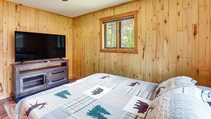 Een slaapkamer met houten wanden, een plafondventilator, een televisie op een houten kast en een raam.