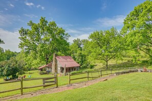 A rustic cabin with a red roof, surrounded by lush green trees and a wooden fence.