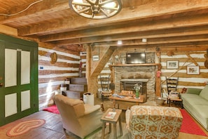 A rustic cabin interior with a stone fireplace, wooden walls, a green door, and a cozy seating area with a sofa and armchairs.