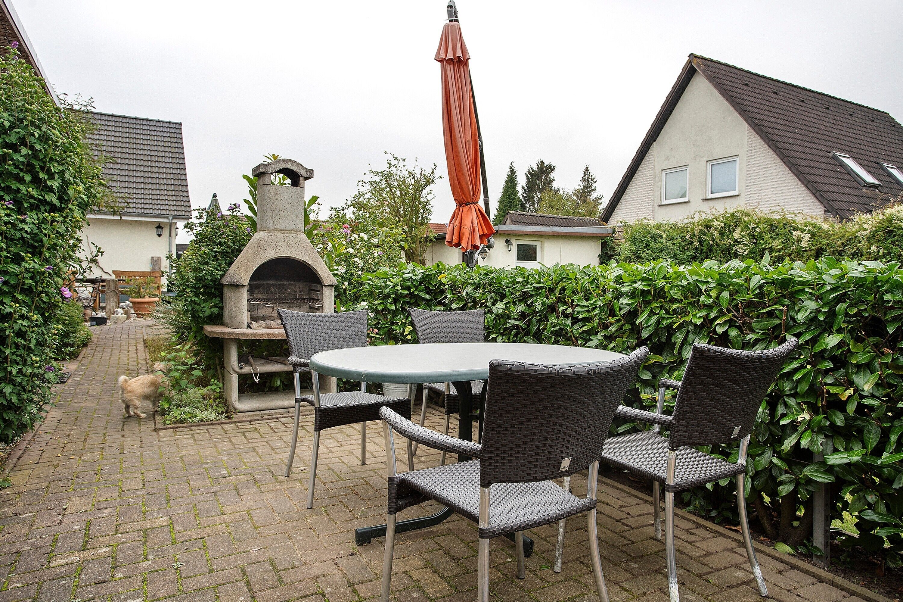 Eine Terrassenfläche mit Tisch und Stühlen, ein Pflasterweg und ein Haus im Hintergrund.