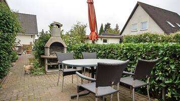 Eine Terrassenfläche mit Tisch und Stühlen, ein Pflasterweg und ein Haus im Hintergrund.