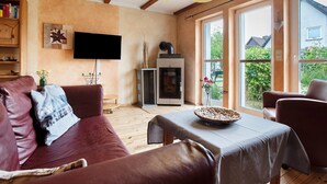A cozy living room with a fireplace, leather sofa, and a dining table with a basket. - Holiday Home 'Ferienhaus Sundperle' with Private Terrace, Private Garden and Wi-Fi (Stralsund)