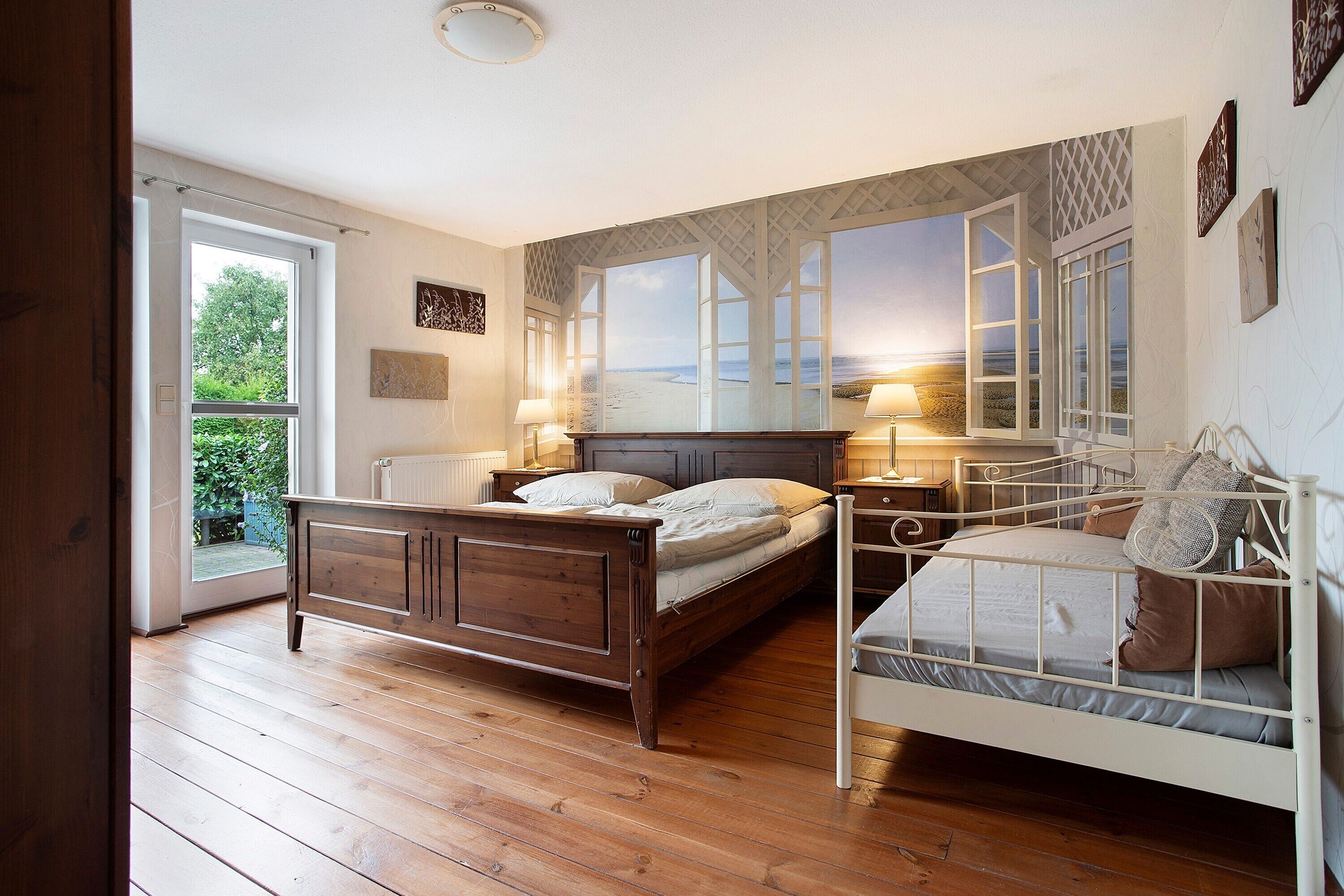 Ein Schlafzimmer mit Holzboden, einem Bett mit Kopfteil, einem Fenster mit Blick auf den Strand und einer Tür, die nach draußen führt.