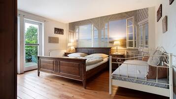 Ein Schlafzimmer mit Holzboden, einem Bett mit Kopfteil, einem Fenster mit Blick auf den Strand und einer Tür, die nach draußen führt.