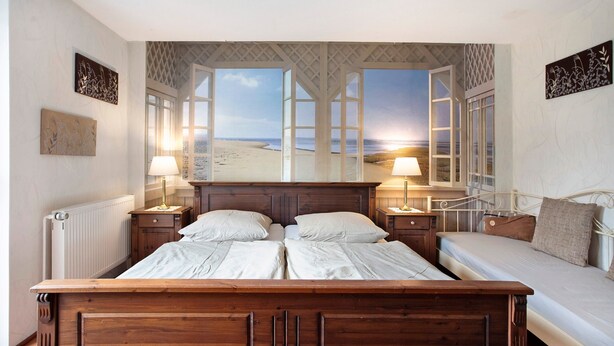 A bedroom with a large bed, two bedside tables, and a view of the beach through open windows. - Holiday Home 'Ferienhaus Sundperle' with Private Terrace, Private Garden and Wi-Fi (Stralsund)