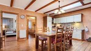 A wooden dining table with chairs, a kitchen with white cabinets, and a clock on the wall. - Holiday Home 'Ferienhaus Sundperle' with Private Terrace, Private Garden and Wi-Fi (Stralsund)