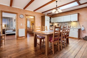 A wooden dining table with chairs, a kitchen with white cabinets, and a clock on the wall.