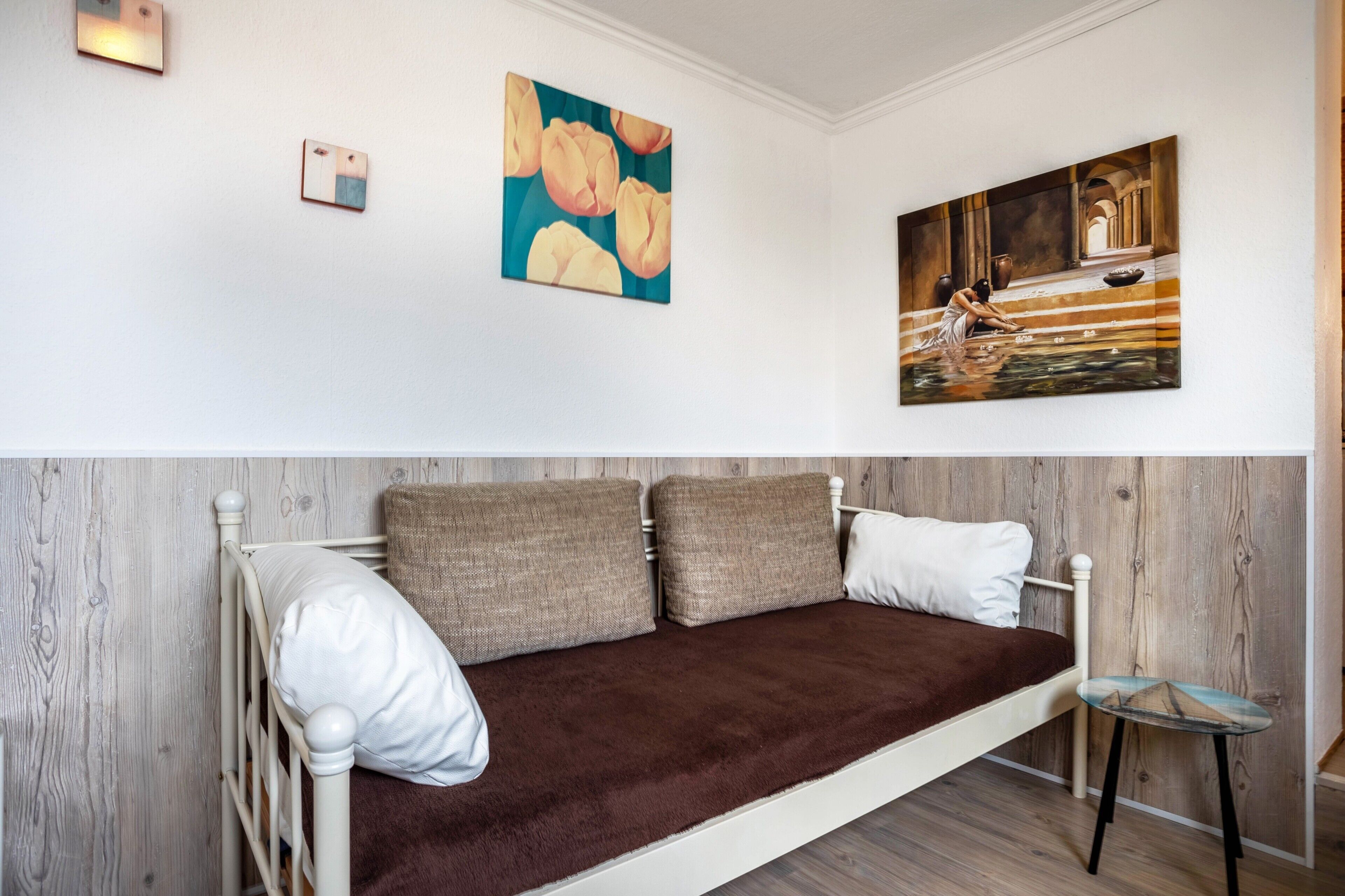 A room with a bed, a small table, and two paintings on the wall.